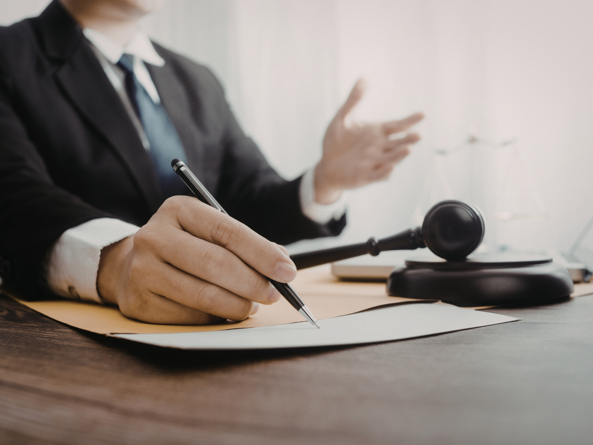 Attorney signing a legal document beside a gavel and scales of justice