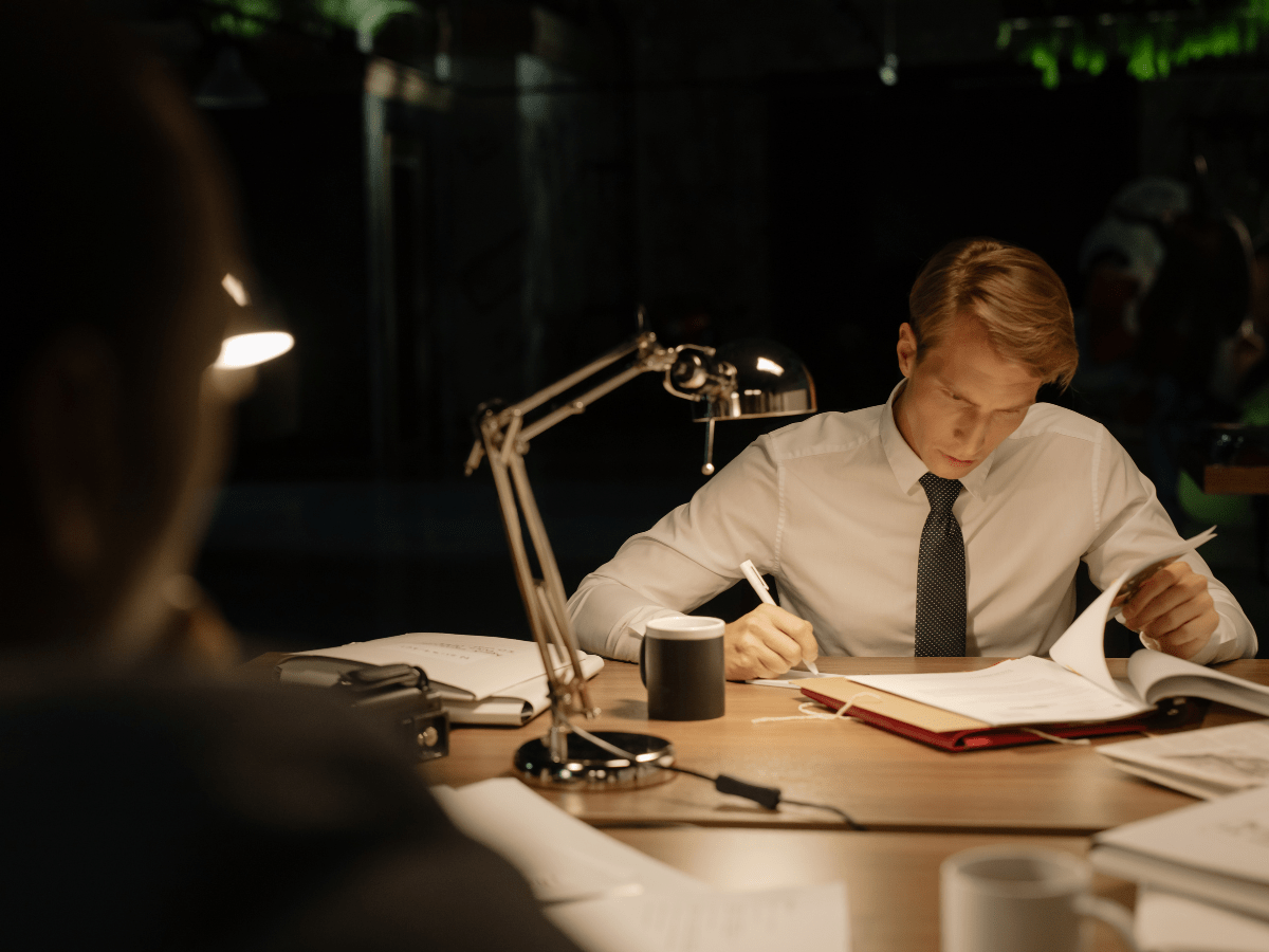 Private investigator reviewing case files late at night under a desk lamp